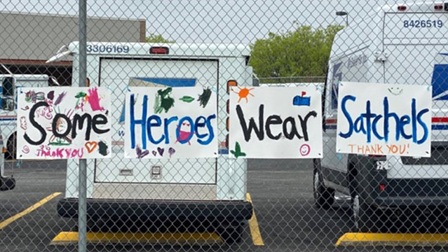 Hand-drawn sign in front of Postal facility saying, 'Some heroes wear satchels, thank you'