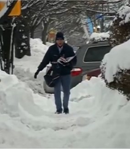 Carrier walks sidewalk during snow storm