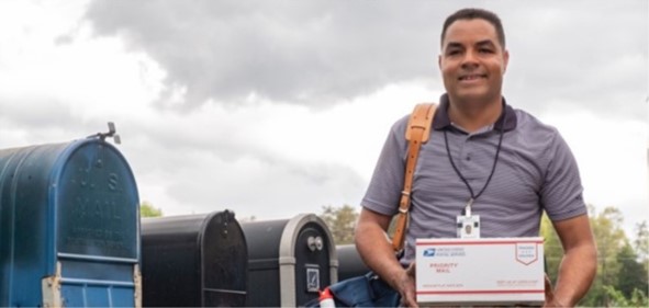USPS Rural Carrier holding package infront of row of mailboxes.