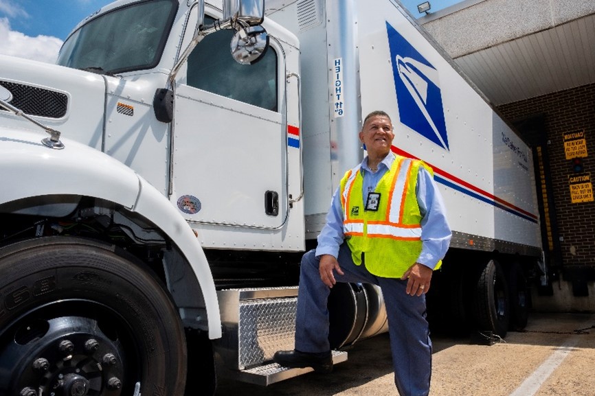 USPS Tractor Trailer Operator in front of a mail tractor