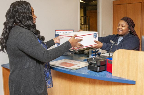 A woman gives her package to an USPS post office employee