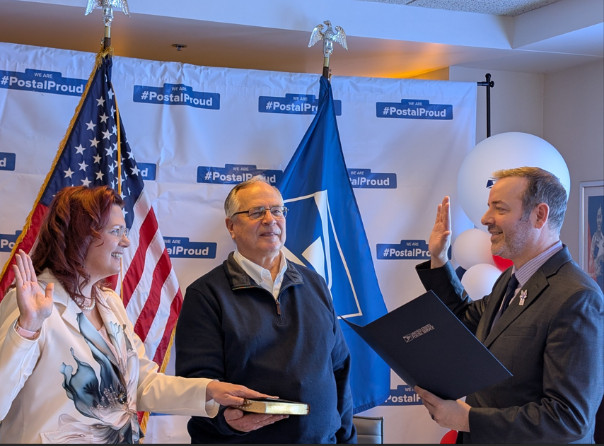 Washington District Manager Trent McNeal (right) swears in the new Littleton, CO Postmaster Andrea Gunnarson as her father Kent Cardwell holds the Bible.