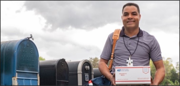 USPS employee in front of mailboxes carrying a Priority Mail package