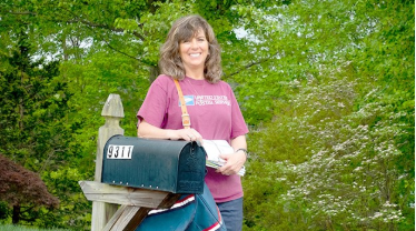A rural carrier standing by a mailbox