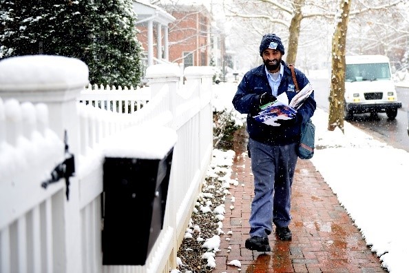 Letter Carrier delivering down a snowy sidewalk