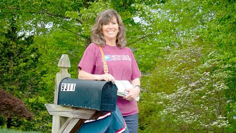 USPS Rural Carrier standing next to a mailbox.