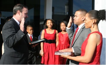 District Manager Dave Fields (l) administers the Oath of Office to Postmaster Anthony J. Spriggs, with wife Denora and their three children at his side.