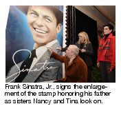 Frank Sinatra, Jr., signs the enlargement of the stamp honoring his father as sisters Nancy and Tina look on.