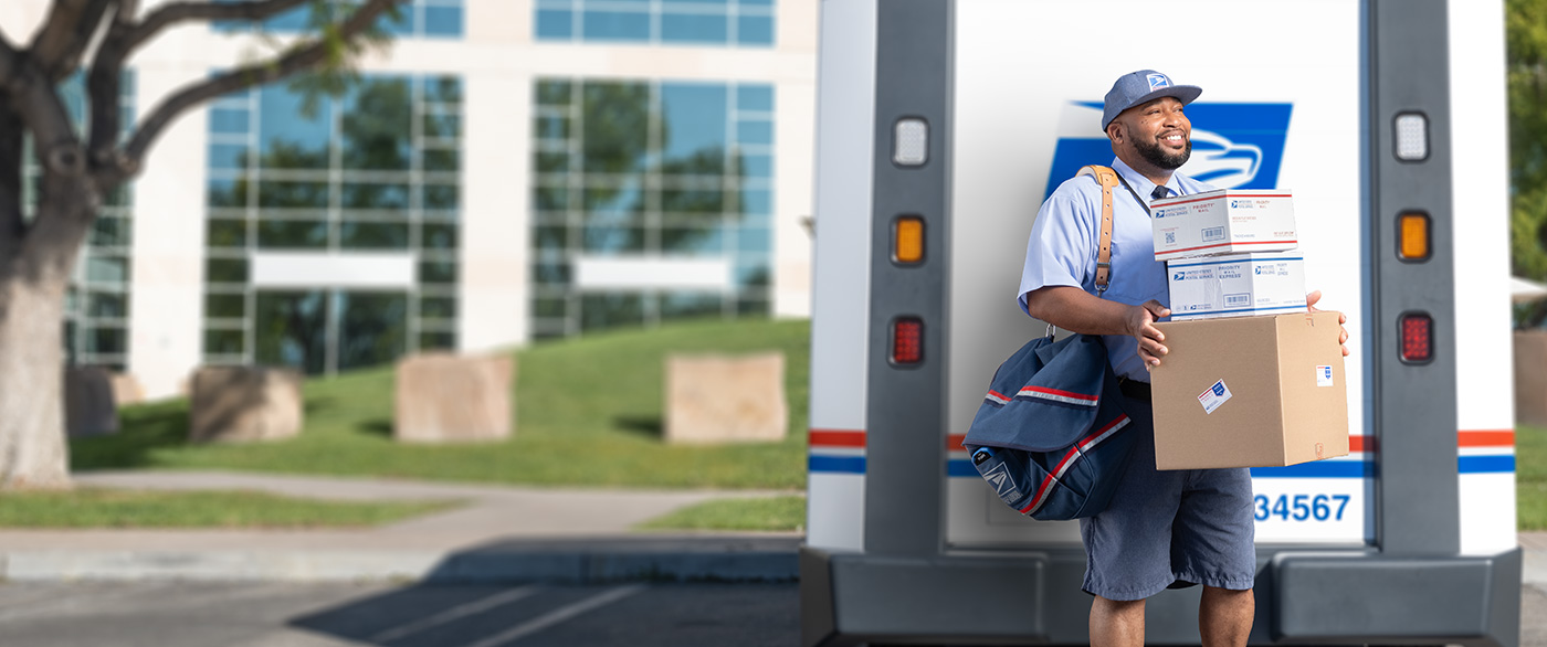 USPS employee carrying mail and packages out of the back of a delivery vehicle while he smiles.