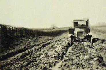 This photograph shows an early 20th century automobile stuck in the mud on a muddy, rutted country road.